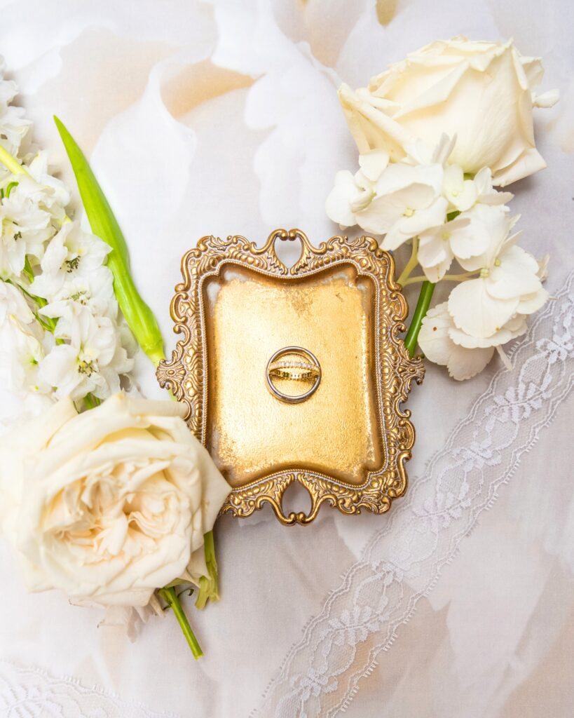 Elegant flatlay of wedding rings styled with white flowers on a lace background for photographers