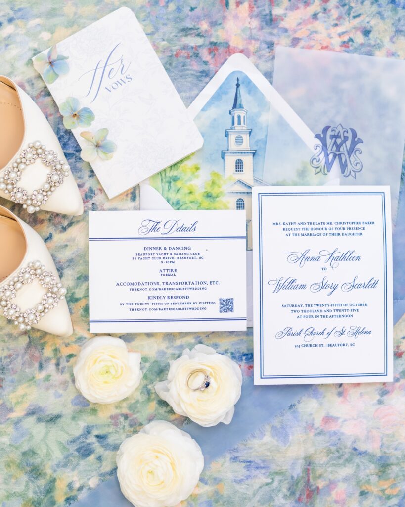 Flatlay of elegant wedding invitation suite styled on a blue mat with white florals