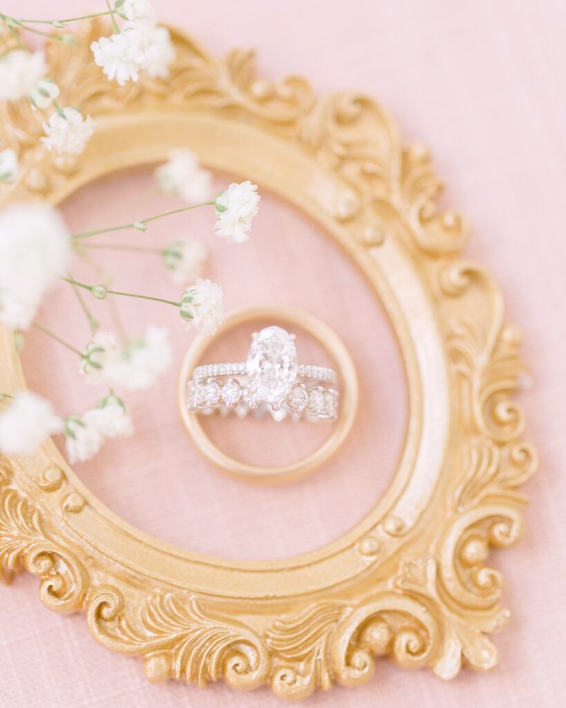 Diamond engagement ring styled in a gold oval frame on a soft pink flatlay mat