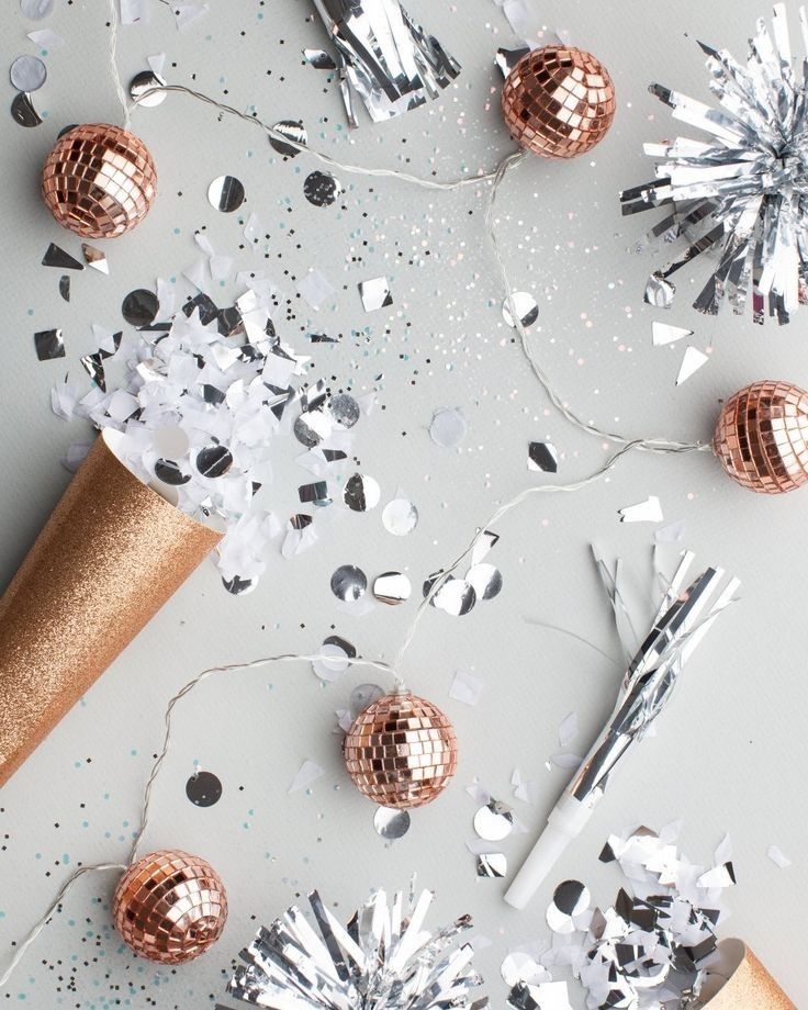 Rose gold disco balls, silver confetti, and party horns on a soft gray background, styled for New Year vision planning.