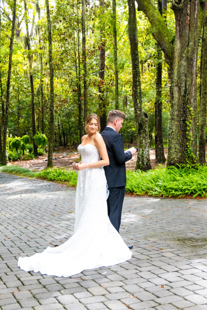 Bride and groom stand back-to-back in a wooded path while reading private vows before the ceremony.