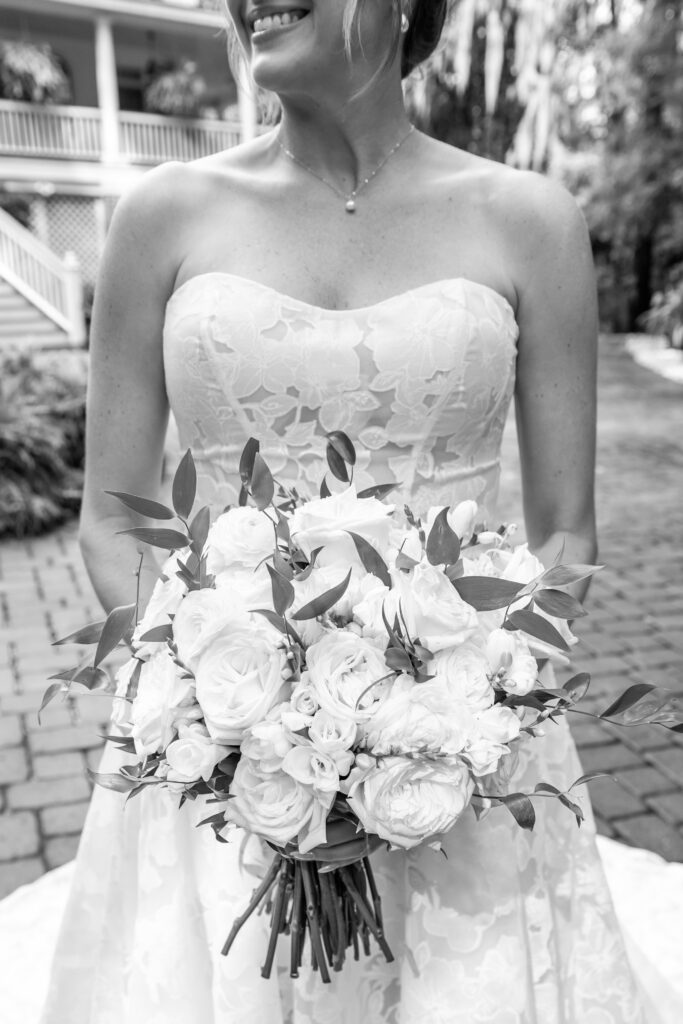 Black-and-white close-up of the bride holding a bouquet of white florals and greenery.