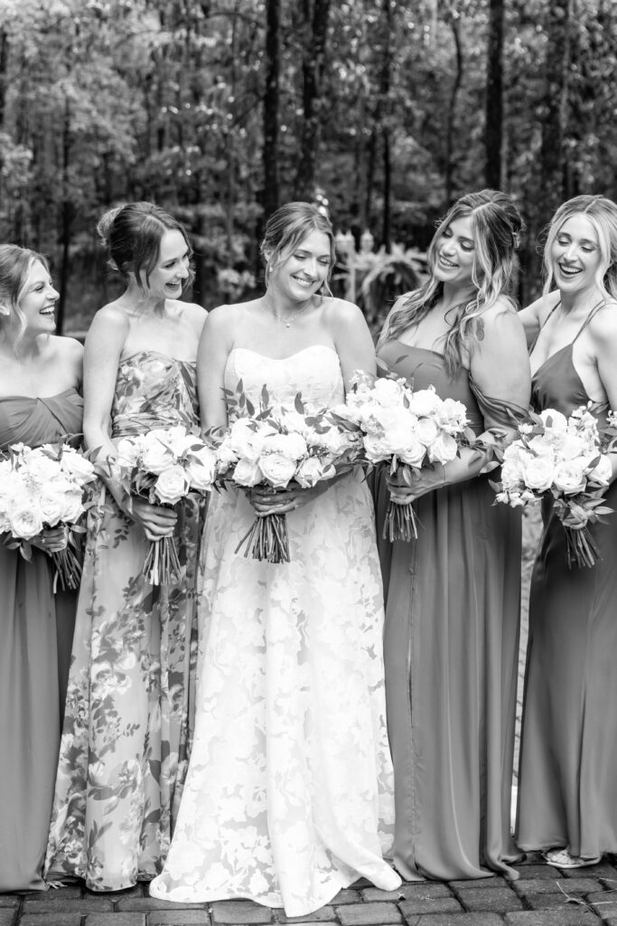 Black-and-white candid of the bride laughing with her bridesmaids holding bouquets.