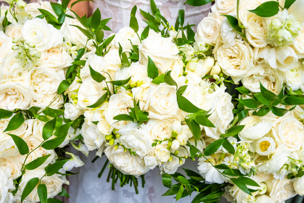 Close-up of multiple white rose and greenery bridal bouquets arranged together.