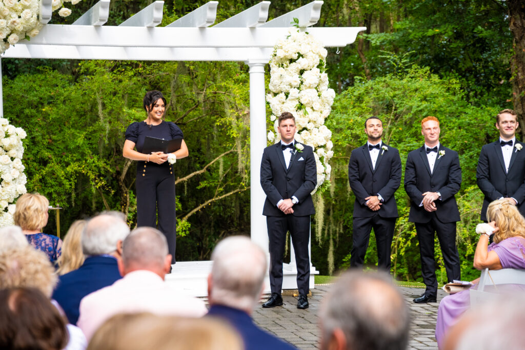 Wedding guests look toward the floral arbor where the officiant and groom stand waiting at The Mackey House ceremony.
