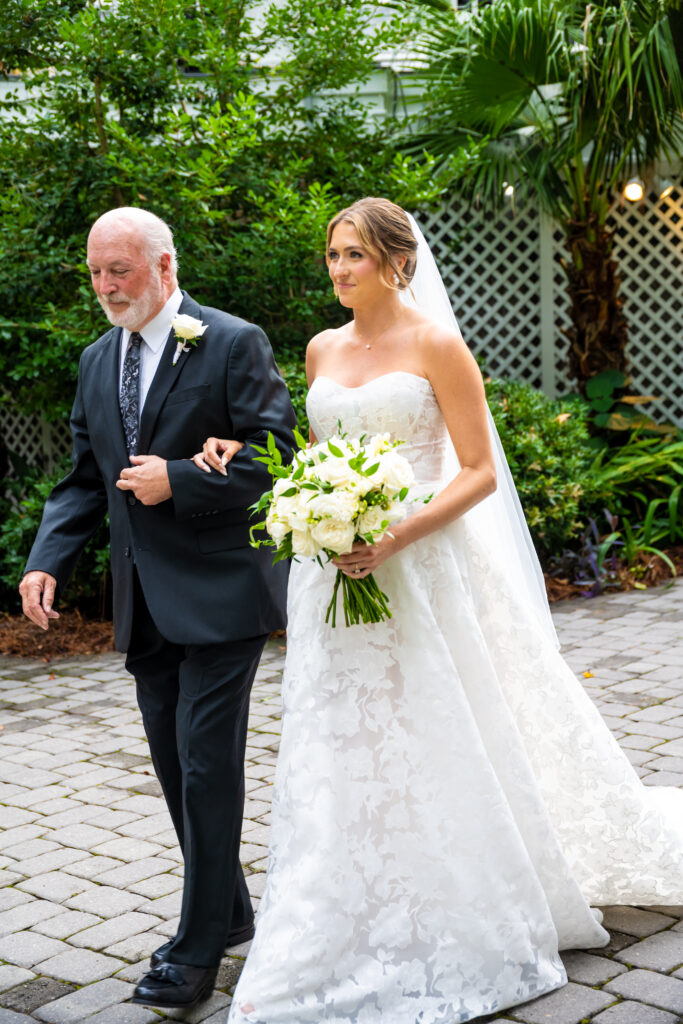 Close-up of bride holding her bouquet as she walks arm-in-arm with her father down the aisle.