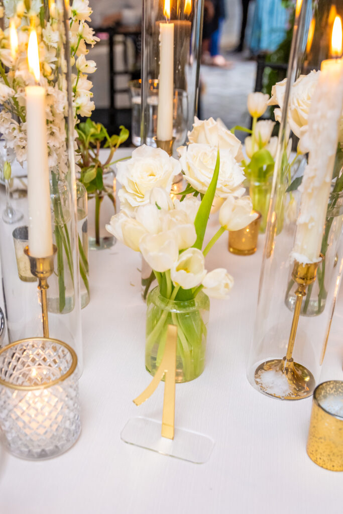 Close-up of white tulips, roses, and candles on a wedding reception table.