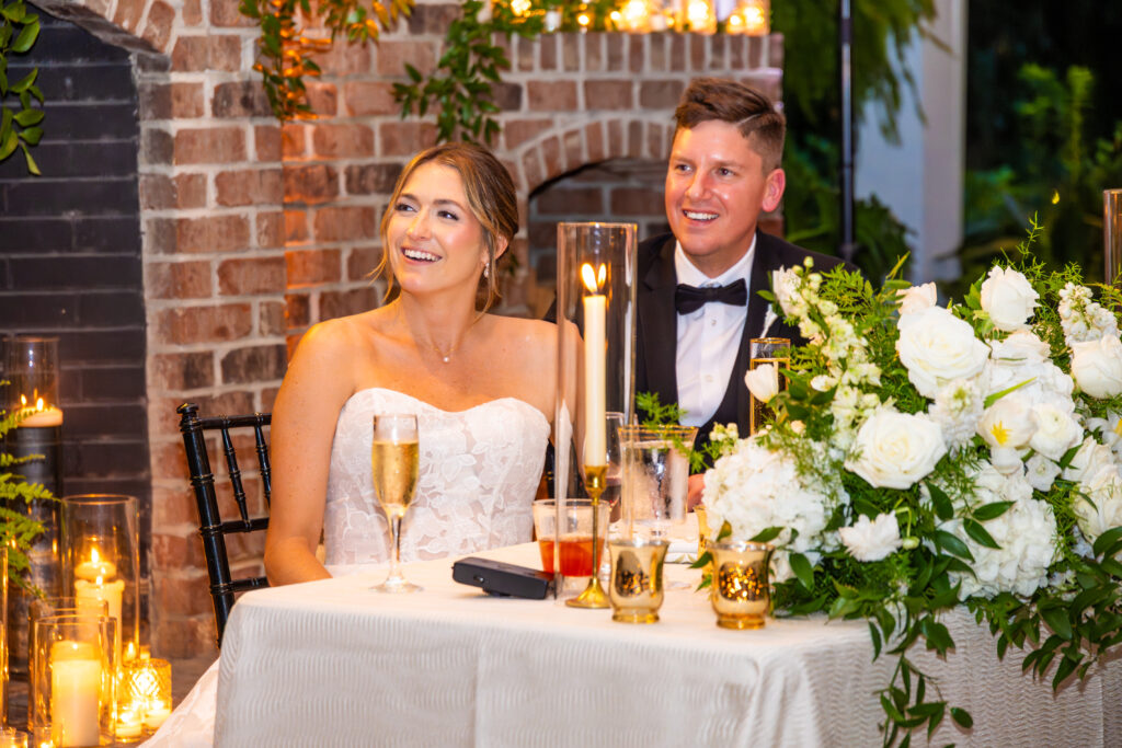 Bride and groom smiling at their sweetheart table during wedding reception toasts.