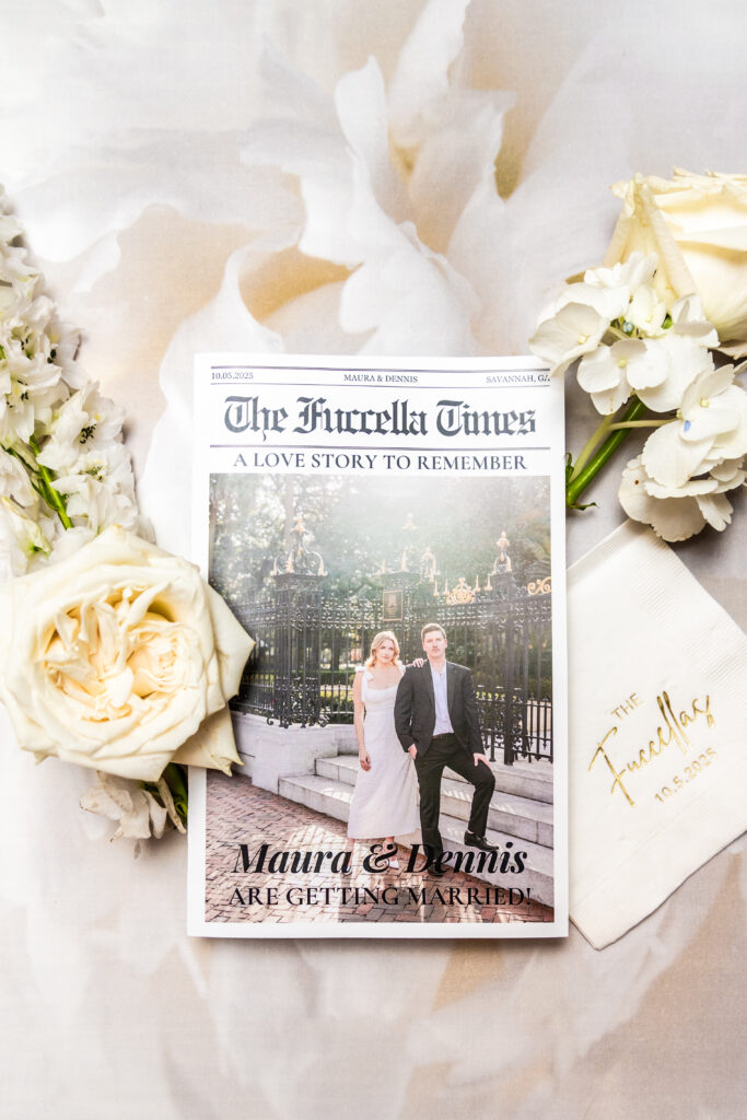 Custom wedding newspaper featuring the couple’s photo, surrounded by white roses and gold-foil napkins.