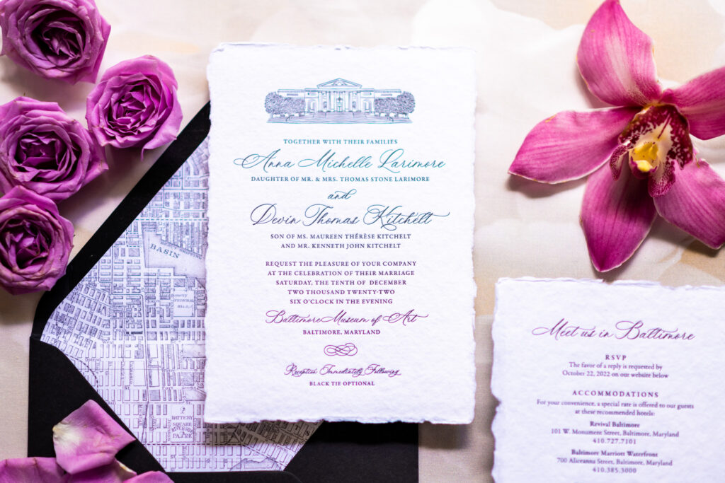 Baltimore wedding invitation suite flat lay featuring a deckled edge invitation with a venue illustration of the Baltimore Museum of Art, a vintage Baltimore city map envelope liner, purple roses, and a pink orchid, photographed by Baltimore wedding photographer Jennifer Mary Collective