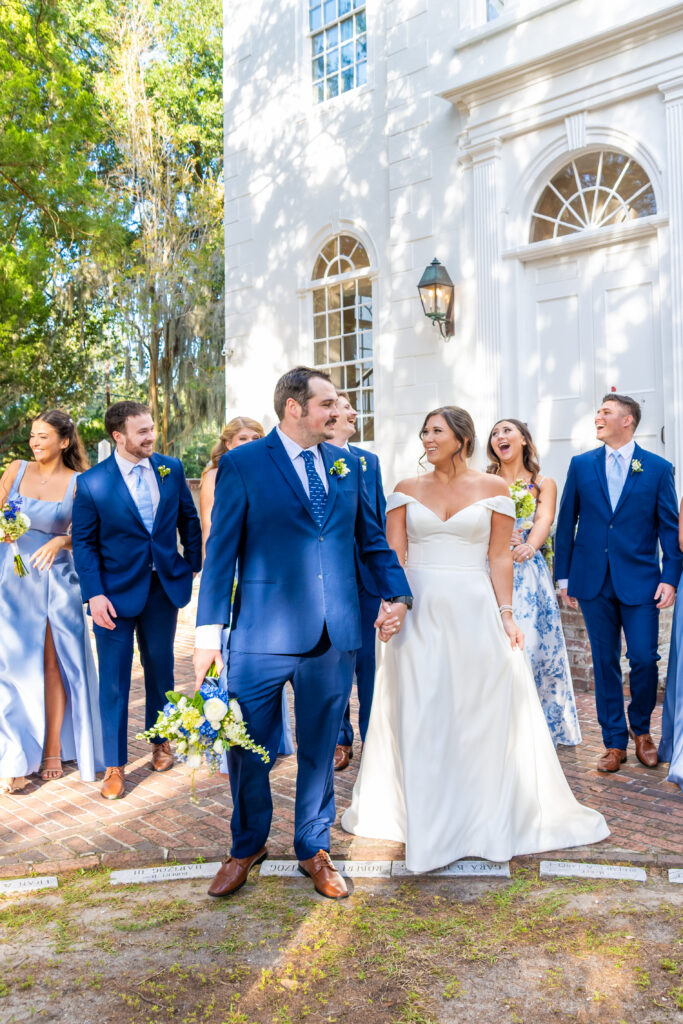 Bride and groom leading their full wedding party while laughing together in front of a white historic building, photographed by Baltimore wedding photographer Jennifer Mary Collective