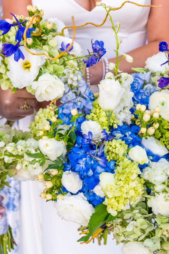 Close up of wedding bouquets featuring blue hydrangea, white ranunculus, green viburnum, white snowberries, and curly willow branches held by a bride, photographed by Maryland wedding photographer Jennifer Mary Collective