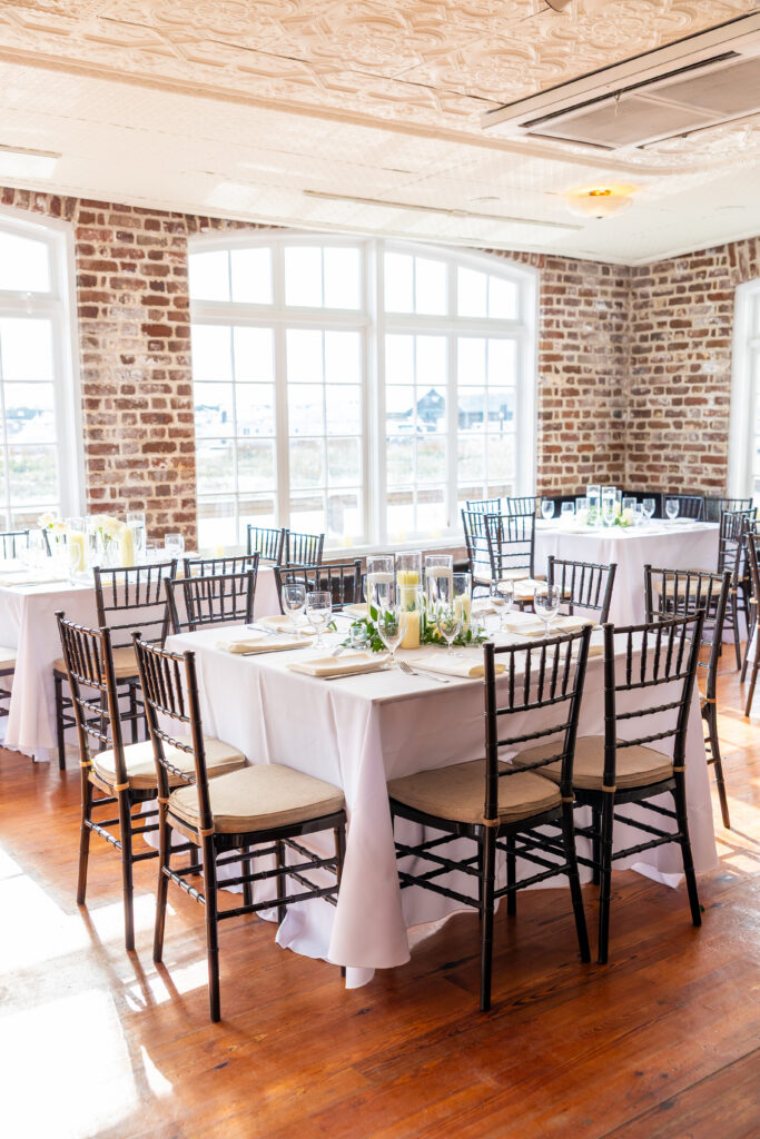 Elegant wedding reception room with white linen tables, black chiavari chairs, exposed brick walls, and tall arched windows, photographed by Maryland wedding photographer Jennifer Mary Collective