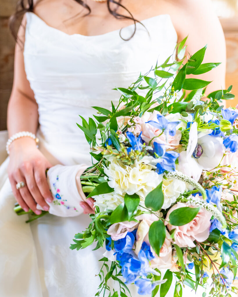 Bride holding a lush cascading bridal bouquet with blue delphinium, blush roses, white anemones, and greenery wrapped with an embroidered floral handkerchief, photographed by Maryland wedding photographer Jennifer Mary Collective