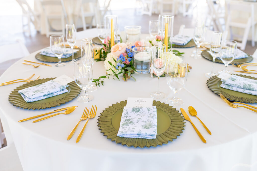 Full round wedding reception table with olive green sunflower charger plates, gold flatware, printed toile napkins, and a colorful wildflower centerpiece with taper candles, photographed by Maryland wedding photographer Jennifer Mary Collective