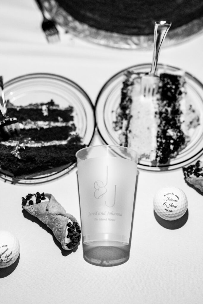 Black and white flat lay of personalized Maryland wedding reception details including a custom pint glass, golf ball favors, cannoli, and slices of wedding cake, photographed by Maryland wedding photographer Jennifer Mary Collective