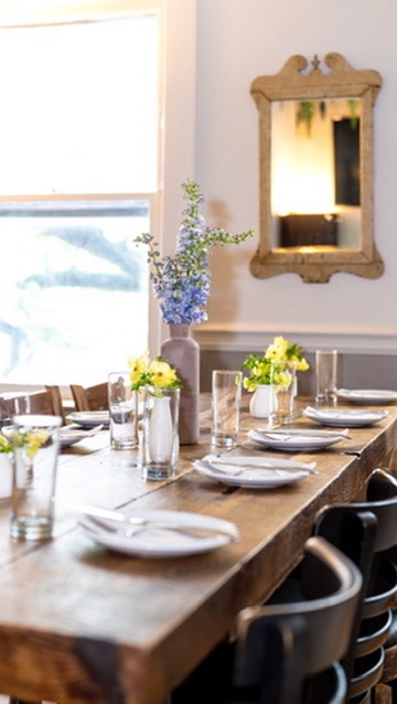 A wooden table set for a Baltimore event vendor community gathering in the Green Room at Verde, with blue and yellow florals, plates, and glassware.